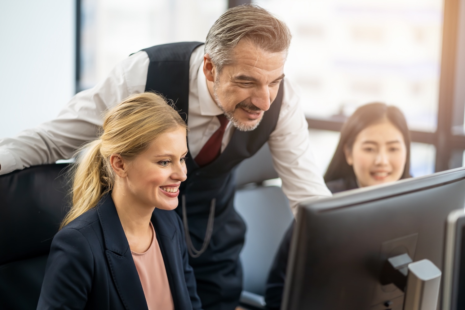 Caucasian male manager giving advice to young female employee in office. Man suggest working instruction while other team members sitting with smile. Happy teamwork, partnership, colleagues concept.